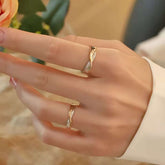 Hand wearing two solid gold intertwined promise rings while touching a peach rose